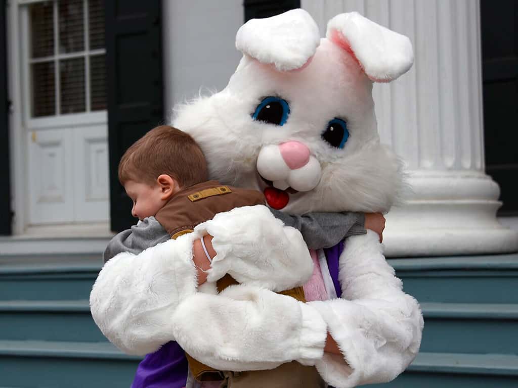 A small child hugs someone dressed up as the Easter Bunny on the front steps of Drumthwacket.