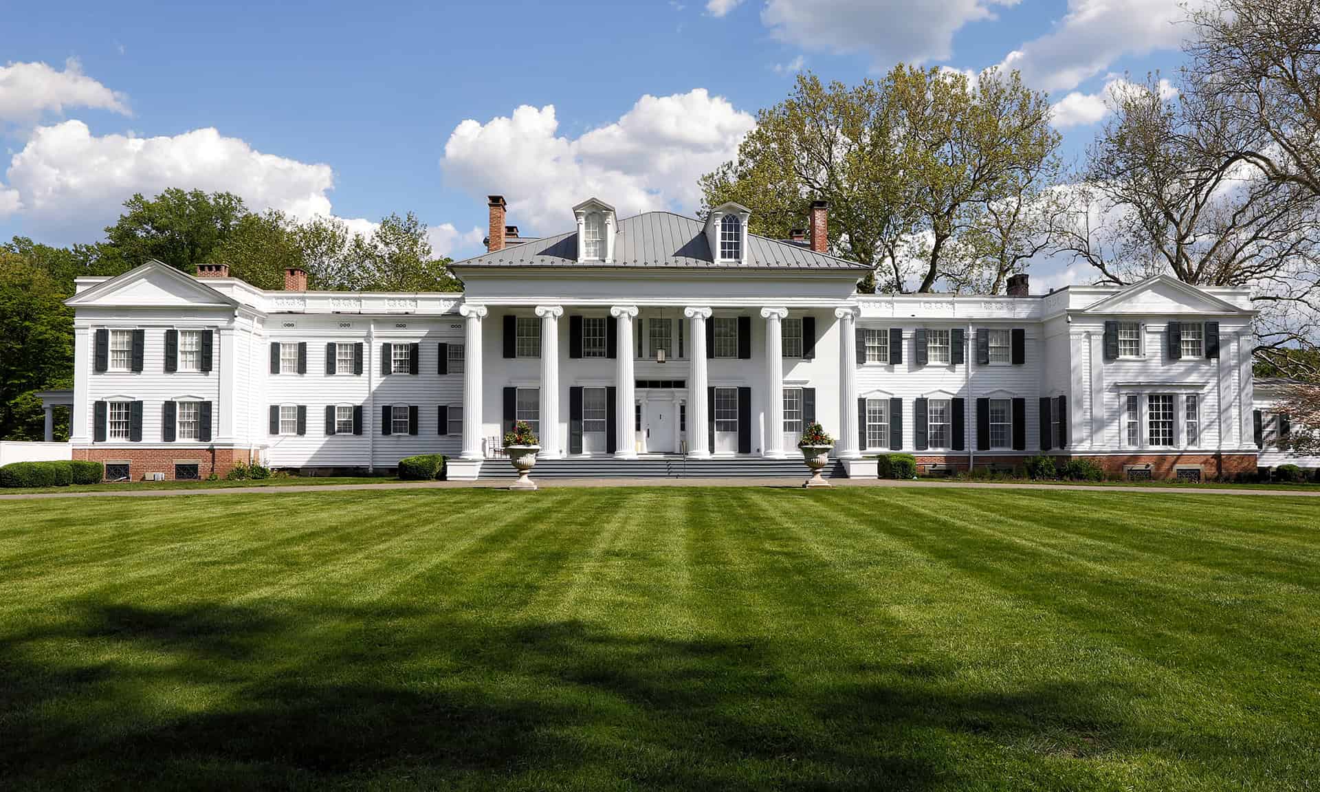 Front exterior of Drumthwacket, the historic official residence of the Governor of New Jersey, surrounded by a spacious green lawn and mature trees.